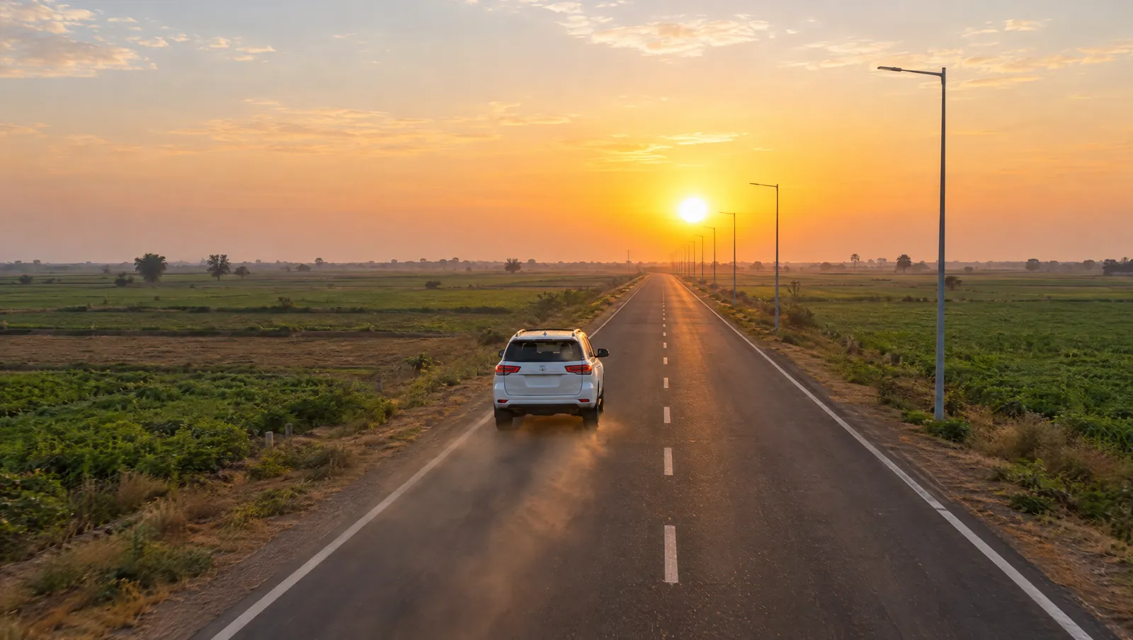 A car driving along a straight new road through flat farmland at sunrise, on the way to a site visit
